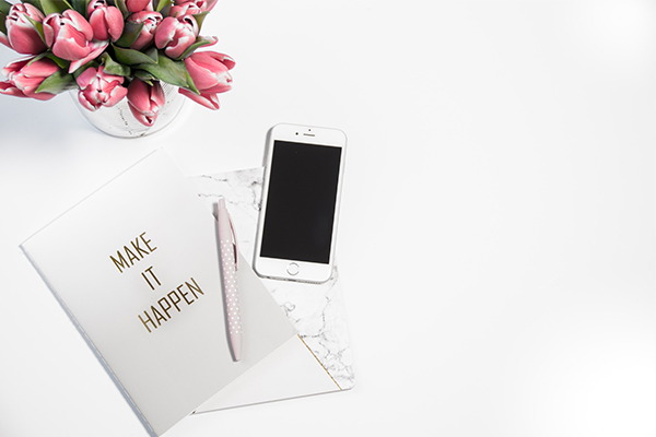 Social Media Coaching: white book with title "make it happen," pen, cellphone, and flower vase on marble counter top
